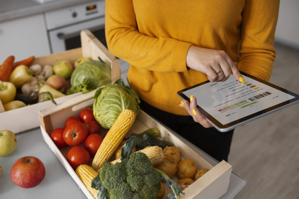una donna con un tablet in mano sta in piedi davanti ad una cassa di verdure, che cercherà di riconoscere tramite l'uso dell'app di food recognition che ha sul tablet.